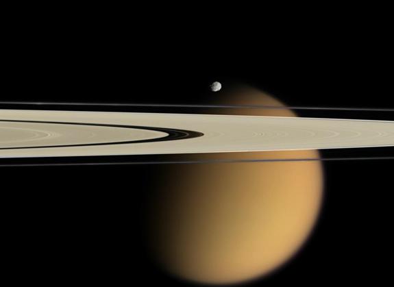Der orange Mond Titan guckt hinter zwei Saturnringen hervor.